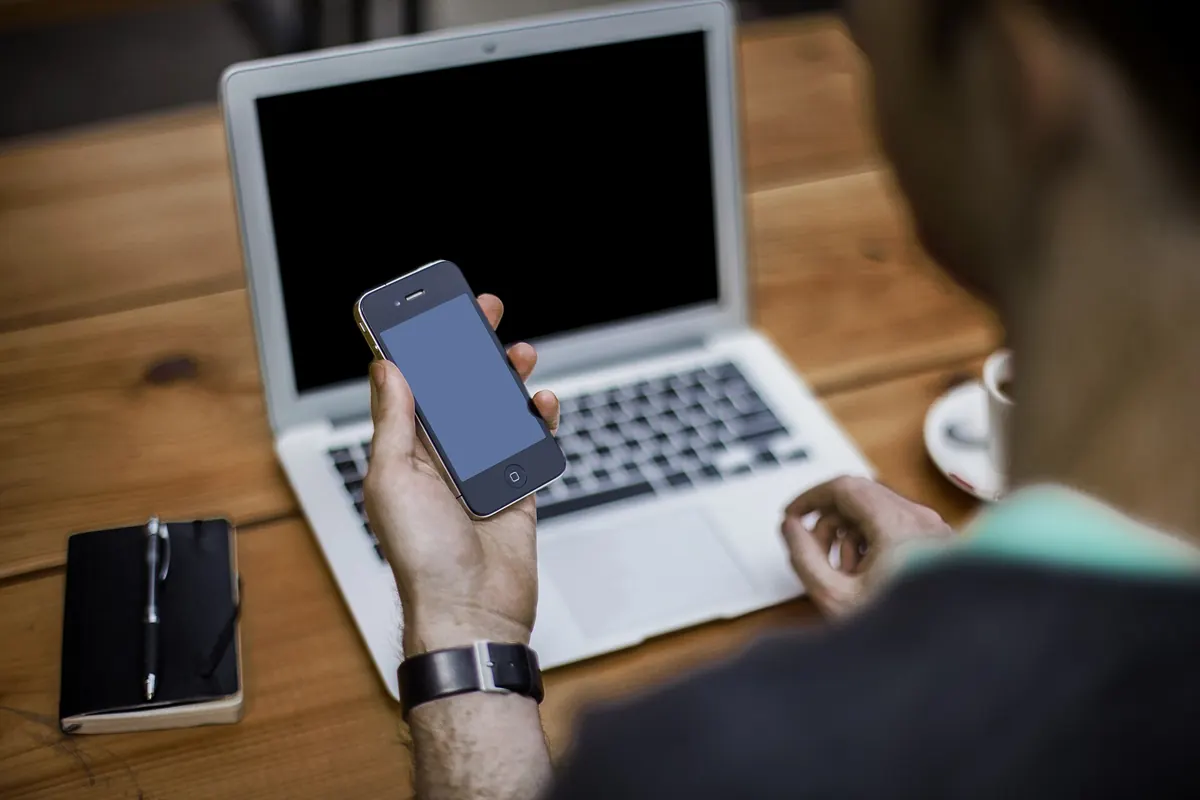 Homme consultant son smartphone devant un ordinateur portable